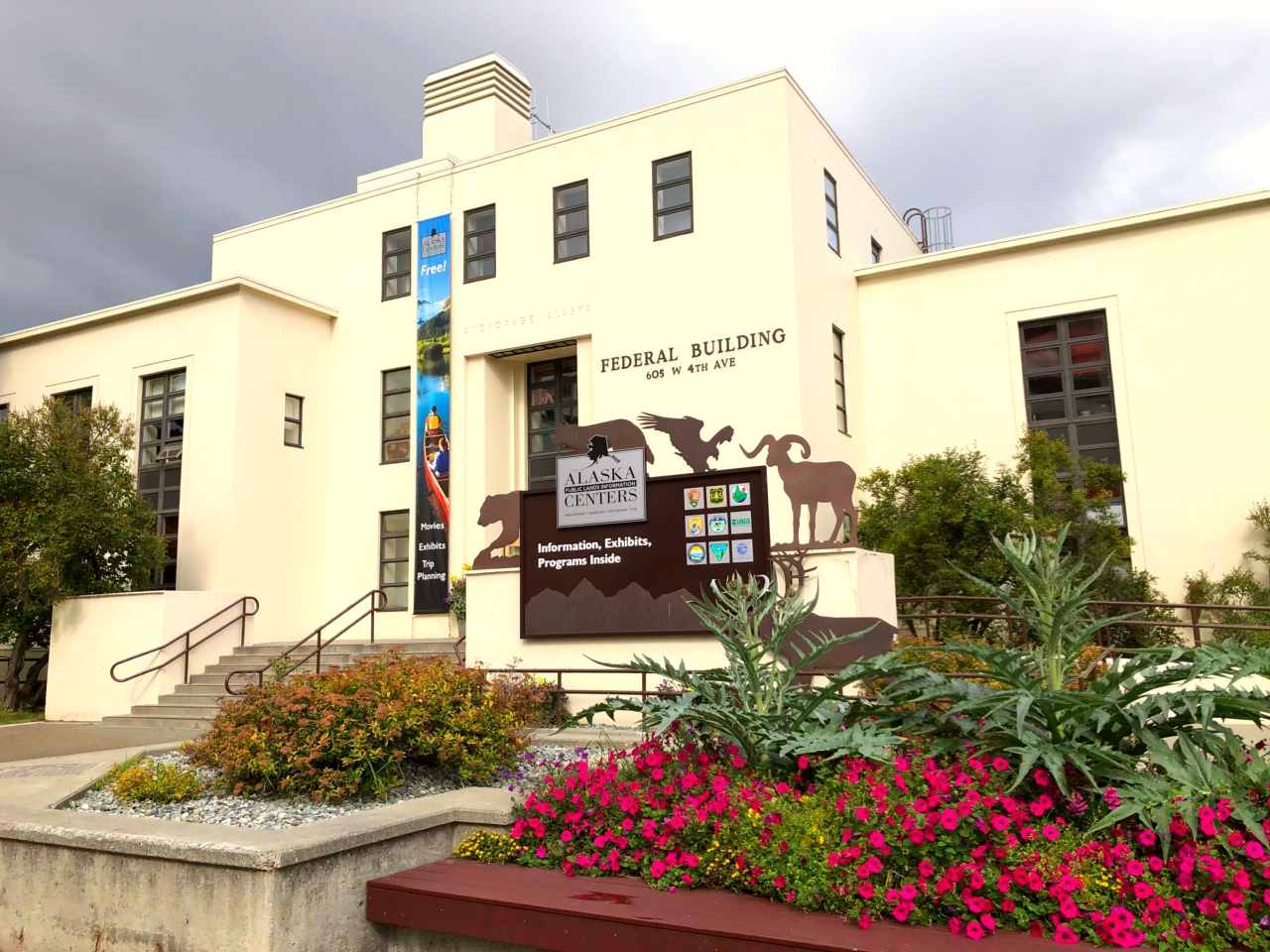 An outdoor view of the Anchorage center, with trees and flowering shrubs in front of the building.