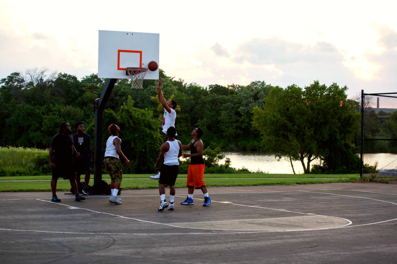 A few men are playing basketball at Anacostia with the Anacostia River in the background.