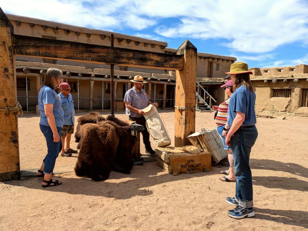 A group of visitors stand around a large wooden apparatus in a plaza courtyard.