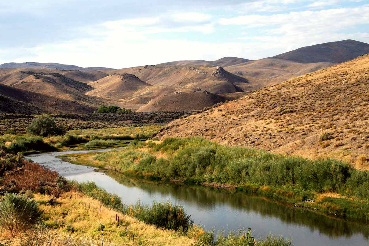 A still creek winds through brown rolling hills.