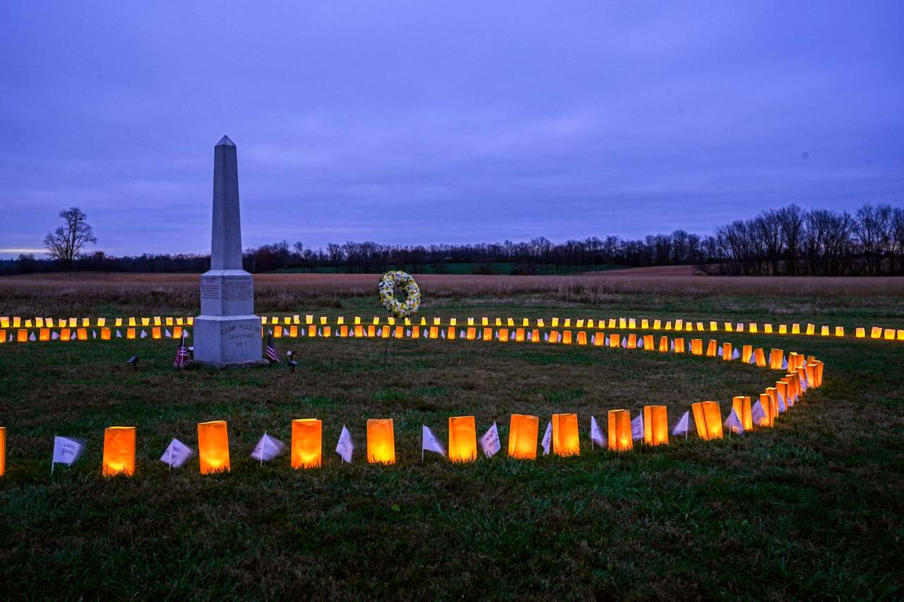 A stone obelisk in a grass field surrounded by luminary bags