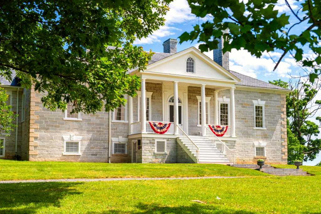 American flag bunting hangs from the porch on a limestone building with a white portico.