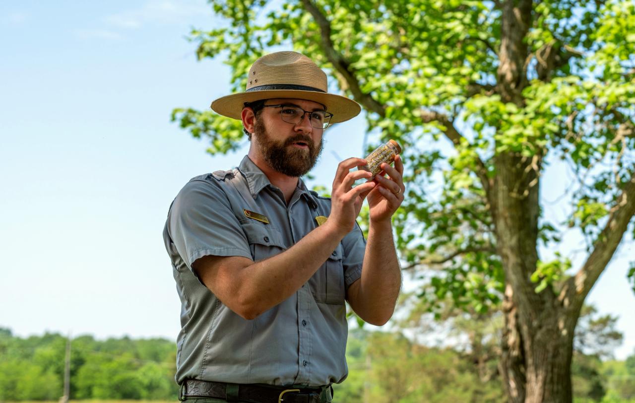 A park ranger holds up a specimen of limestone as he speaks outdoors.