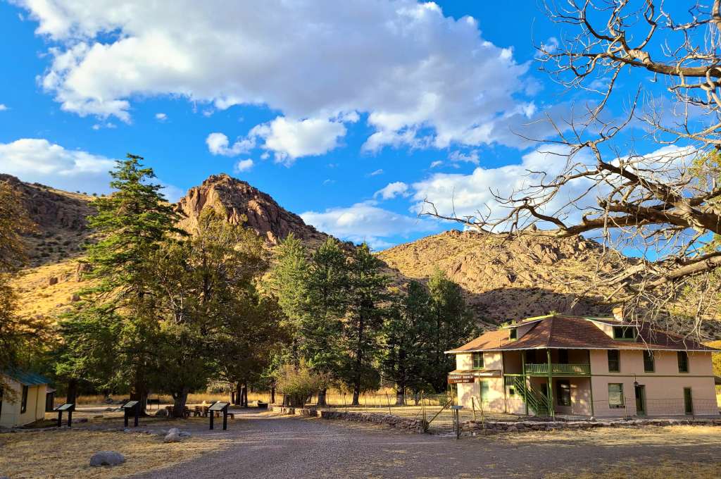 A ranch house in a green field surrounds by low mountains