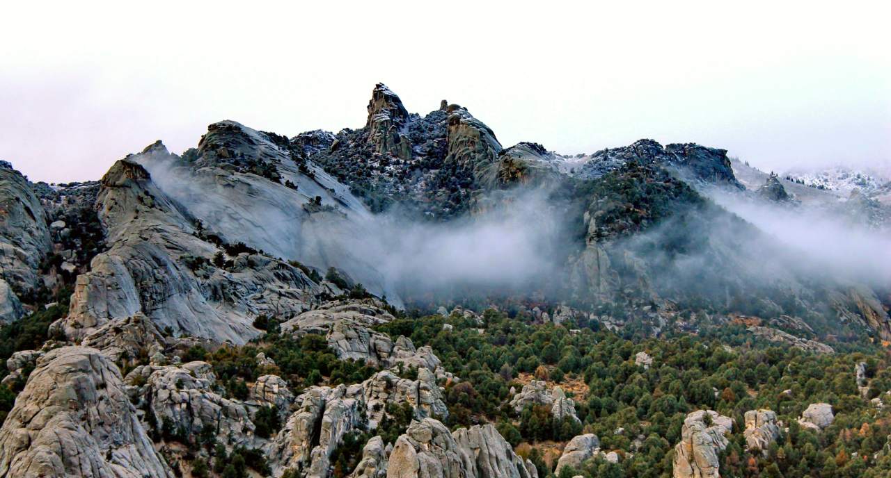 Snow dusted granite formations jut up from a mountainous juniper covered landscape.