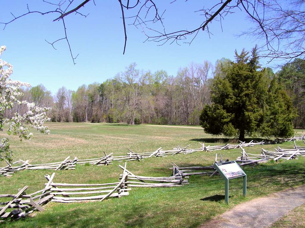 Wooden split rail fencing and flowering trees surround a grassy field behind an interpretive panel