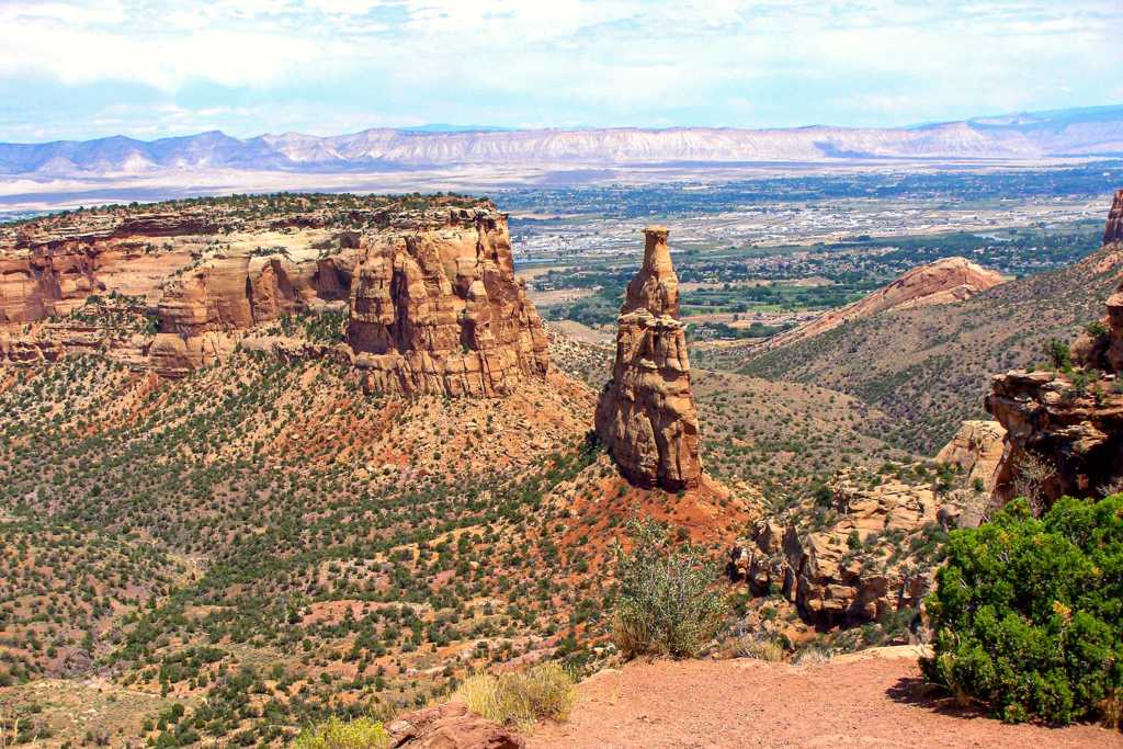 sandstone spire hundreds of feet tall stands above sparsely vegetated canyon bottom and cliffs