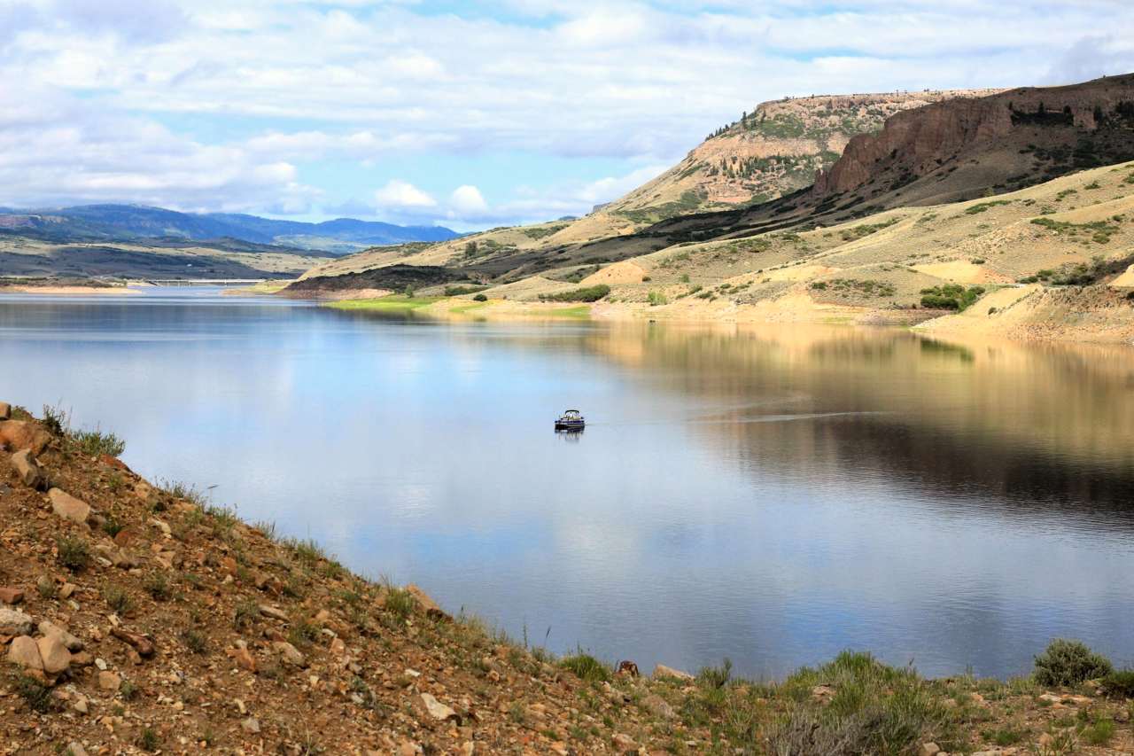 A single boat floating out in a reservoir. Mesas surrounding the area are reflected on the water.