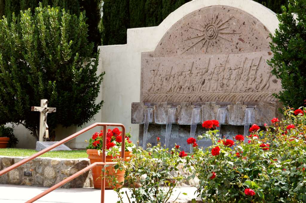 Red roses bloom near a fountain and grave marker