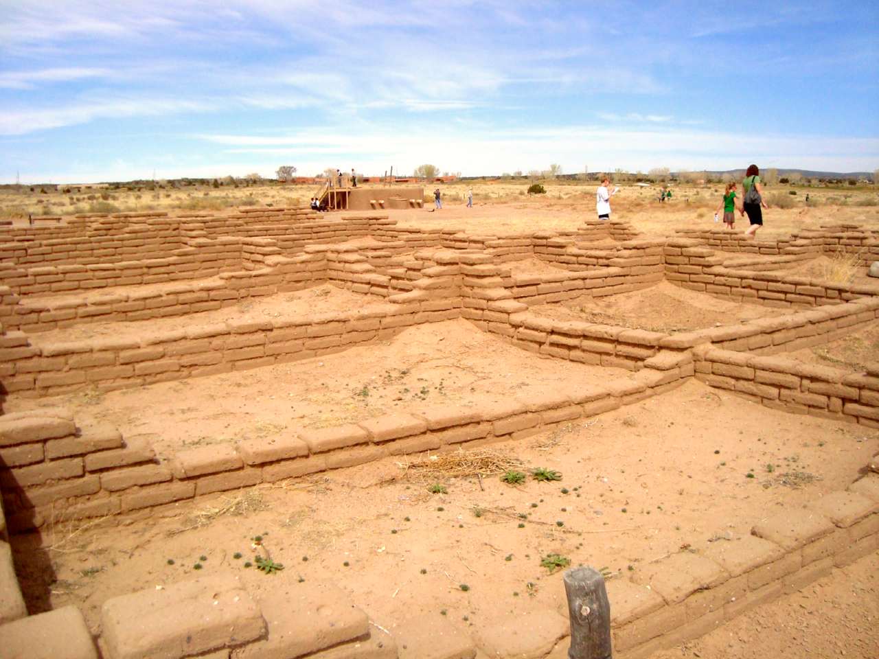 tan-colored pueblo Indian ruins with blue sky and three people