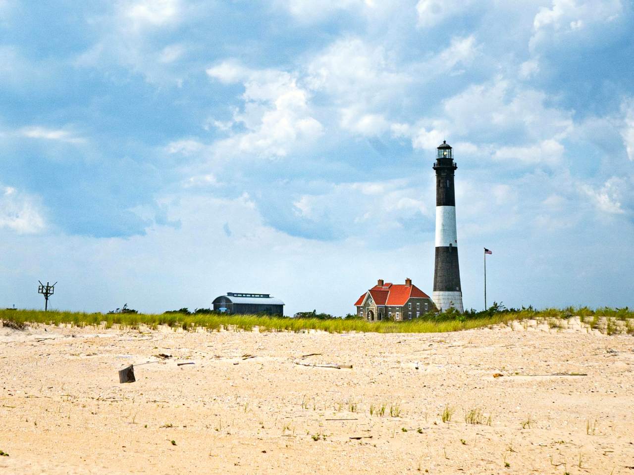 A wide shot of the white and black striped Fire Island Lighthouse from the beach.