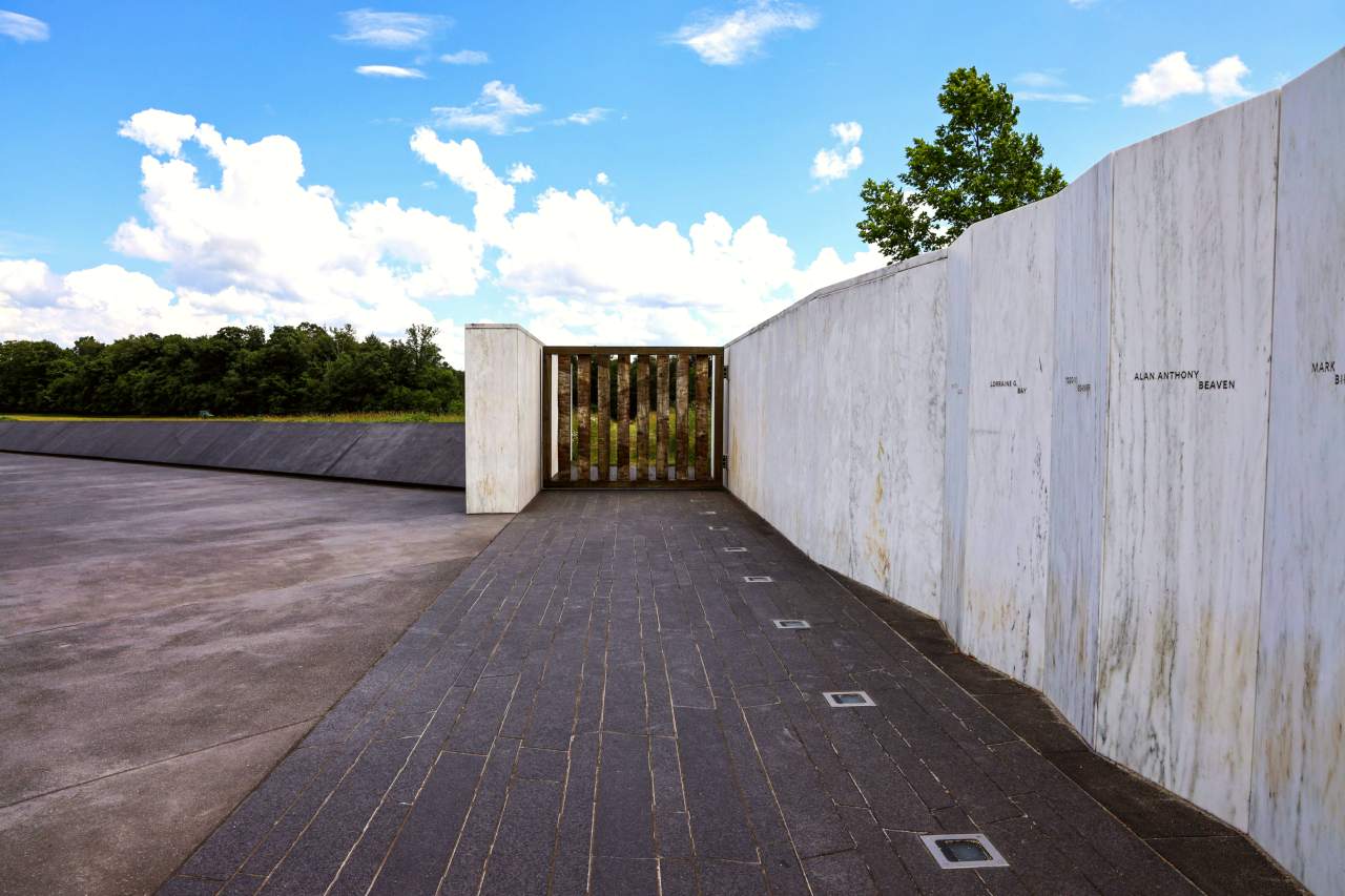 A white marble wall with names engraved on the the walls and the Ceremonial Gate. Blue sky above.