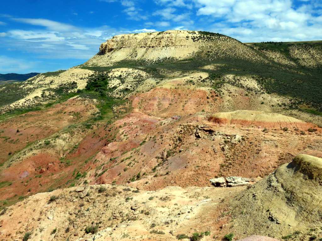 Hills with tan and red sediments partially covered with green vegetation.