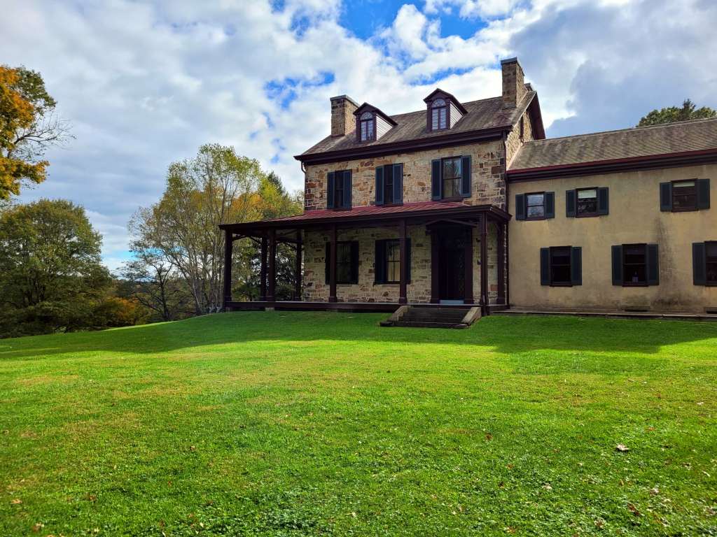 front view of historical Stone House and Visitor Center with green grass lawn with trees and clouds