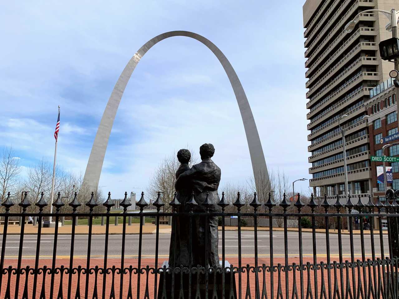 statue of a woman and man embracing in behind a black iron gate in front of the Arch
