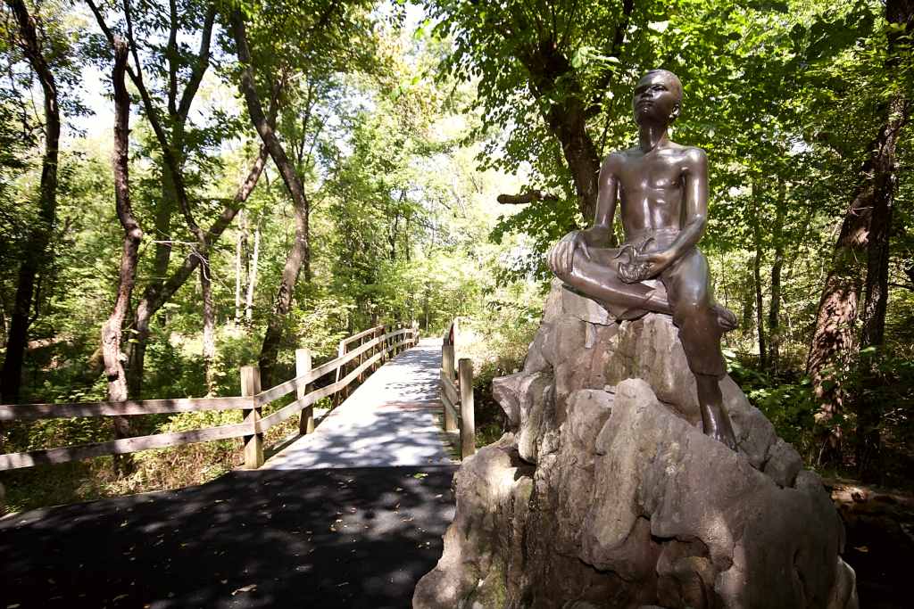 Bronze status of young George Washington Carver atop a large boulder, on the Carver trail.