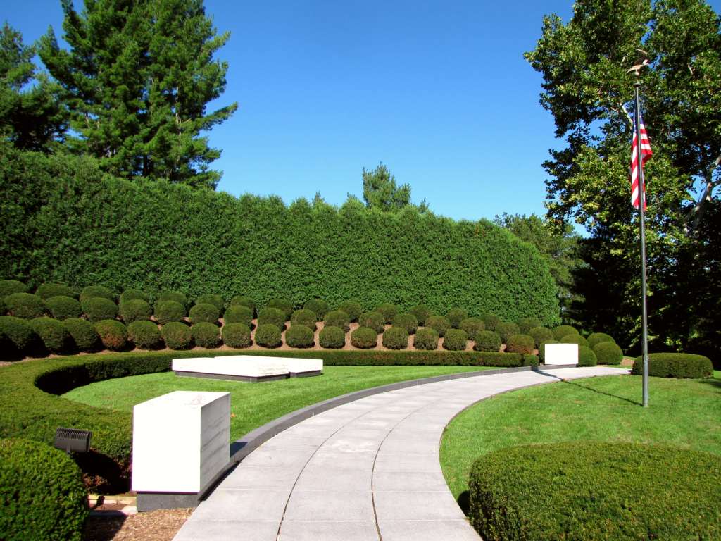 Two marble ledger stones each mark a grave in a semicircular landscaped plot with a flagpole.