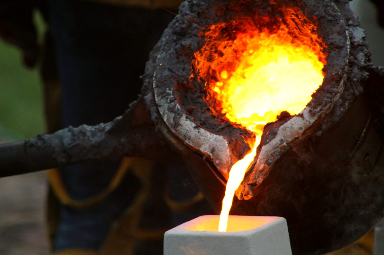 Melted iron pouring into a mold from a metal bucket.