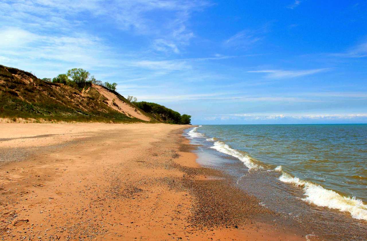 Michigan Lake beach with green grassy dunes in the background, under a blue sky.