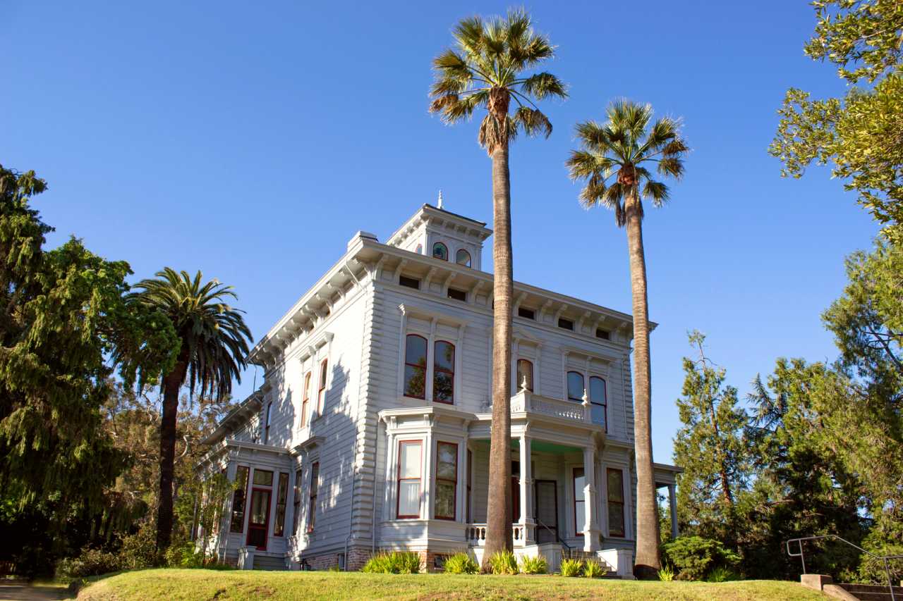 White two story house capped by a bell tower and ringed with palm trees