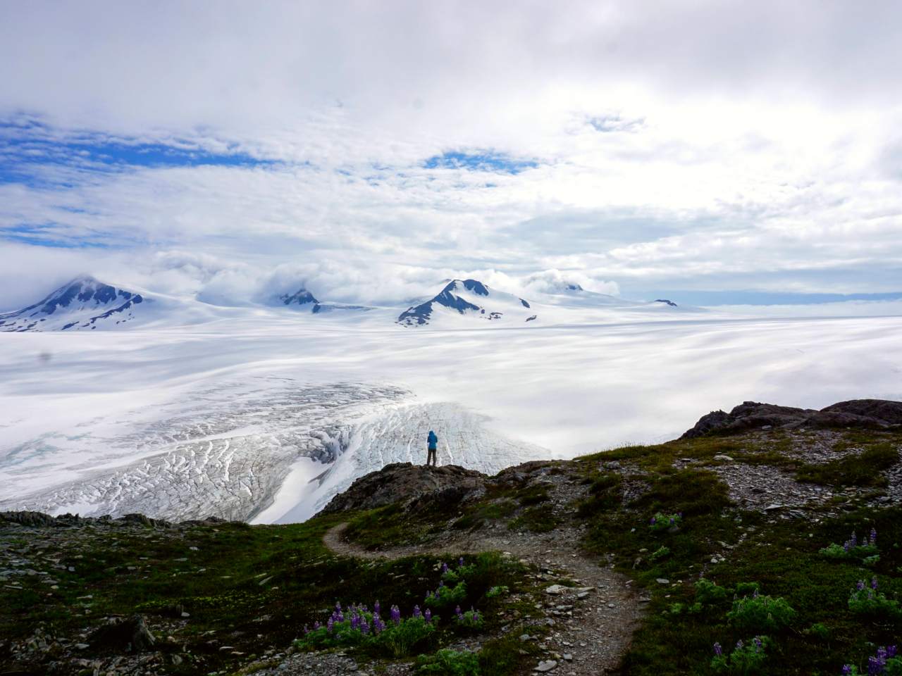A person looks out over a view of snow, ice, and mountain peaks