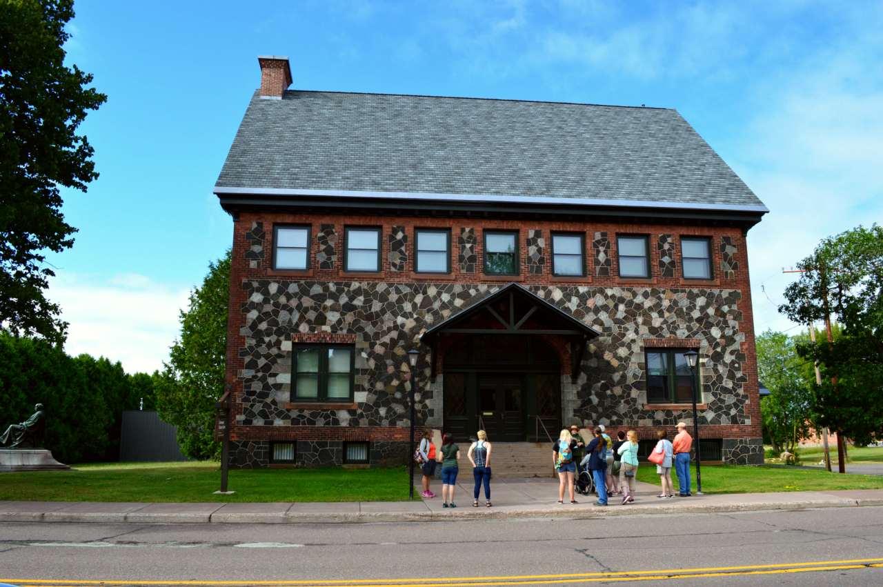 Two story stone and brick building. a ranger leads a group of visitors in front or the steps