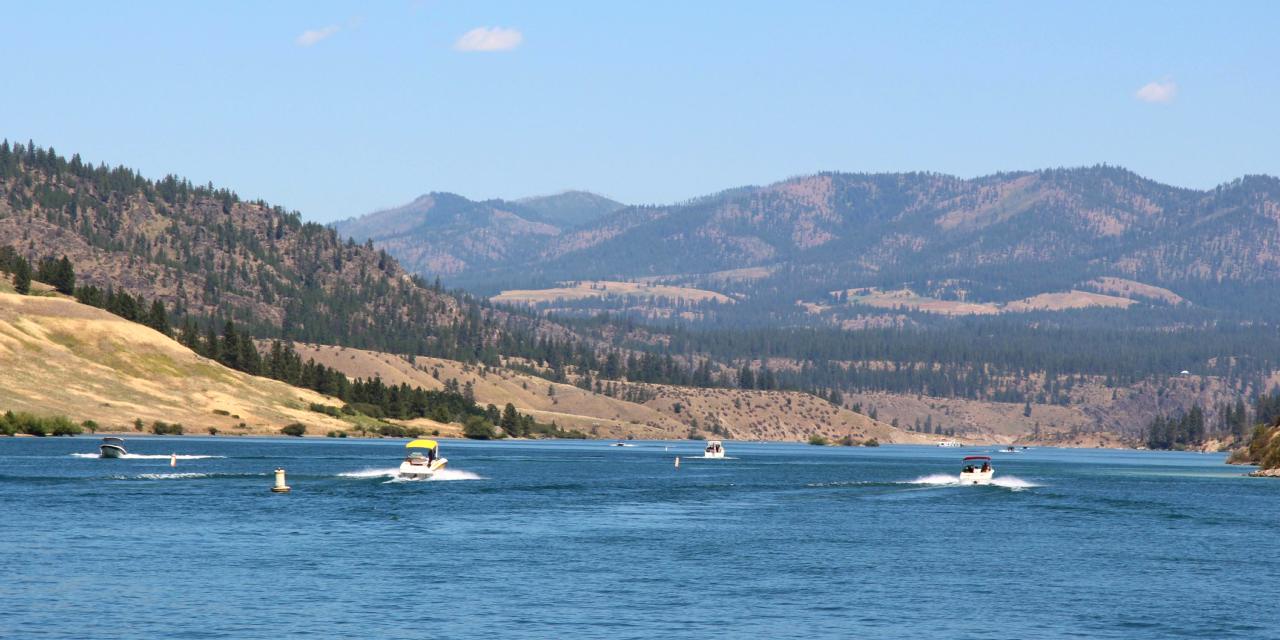 Various motorboats on a blue lake, landscaped by tall tree filled hills.