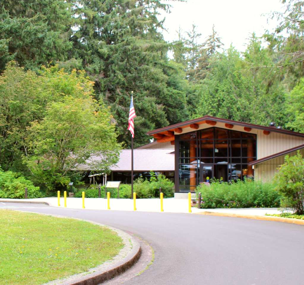 The Fort Clatsop Visitor Center, the front covered in large windows and large trees surrounding it.