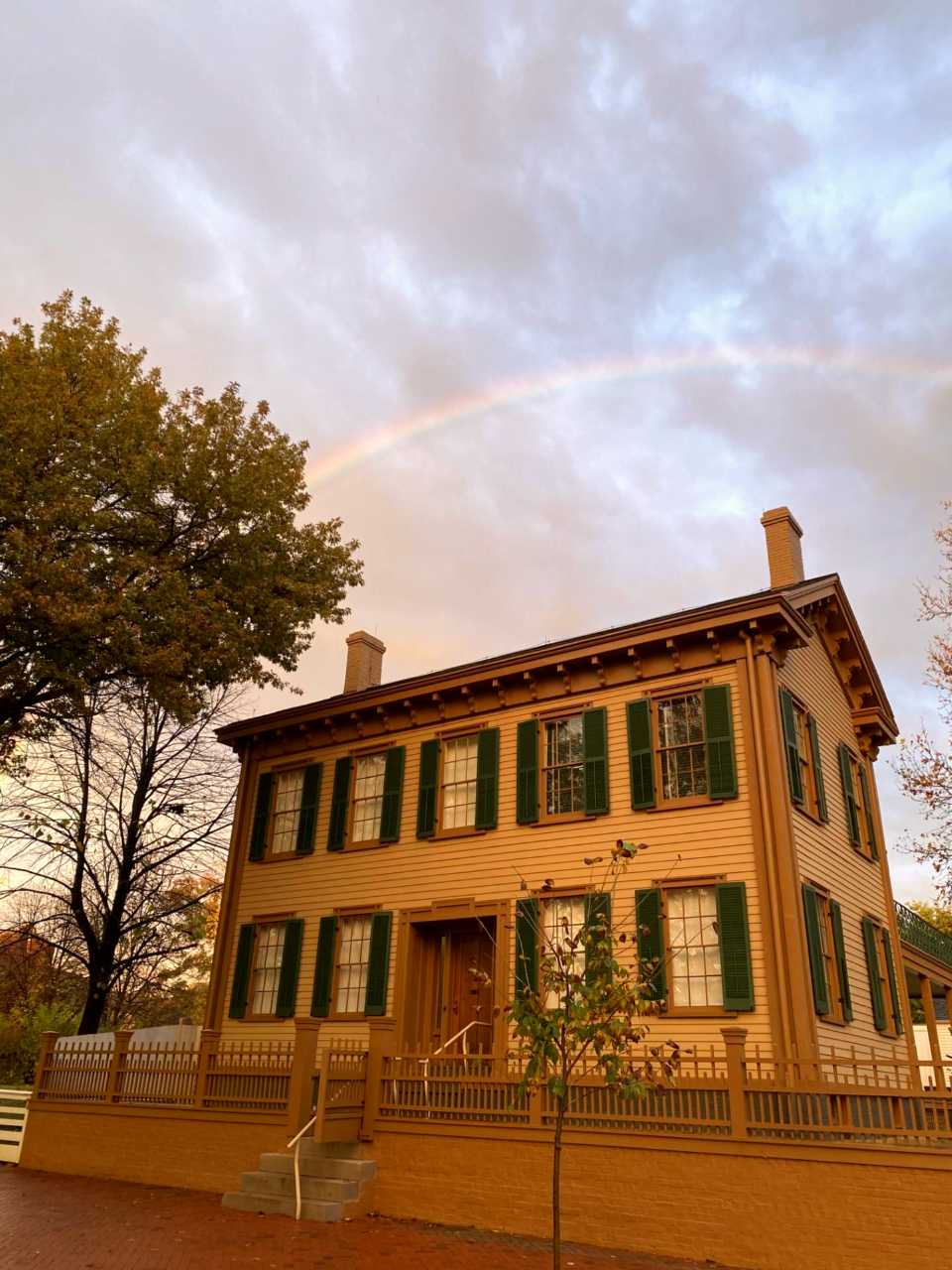 The two-story, tan Lincoln Home with a rainbow in the sky above it.