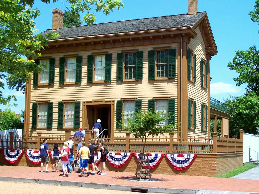 A guide leading a group into the Lincoln Home which has bunting on the front.