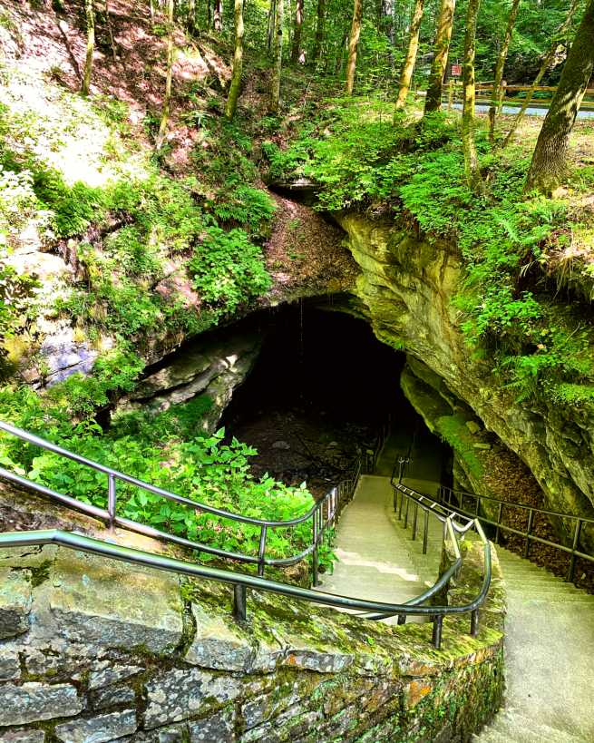 A long staircase travels down a slope into the dark cave opening.