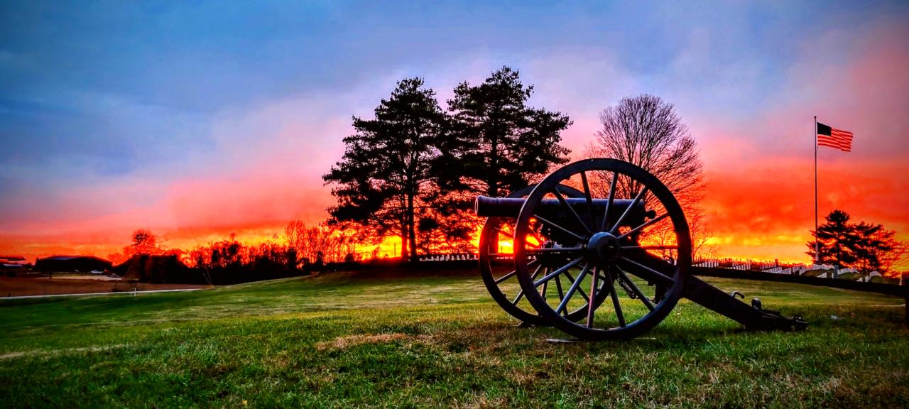 A orange sunset over the white granite headstones in the national cemetery with silhouetted cannon.