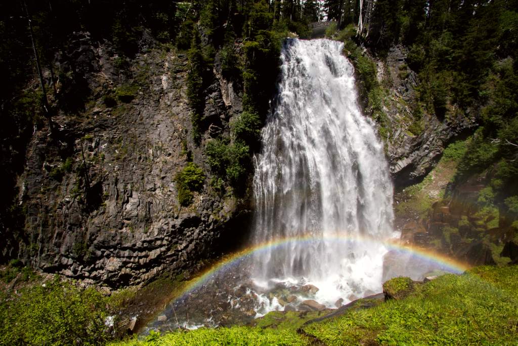 A fan-shaped waterfall cascades over lava cliffs with a rainbow in its mist.