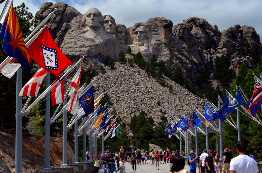 Visitors walking along the Avenue of Flags with Mount Rushmore in the background.
