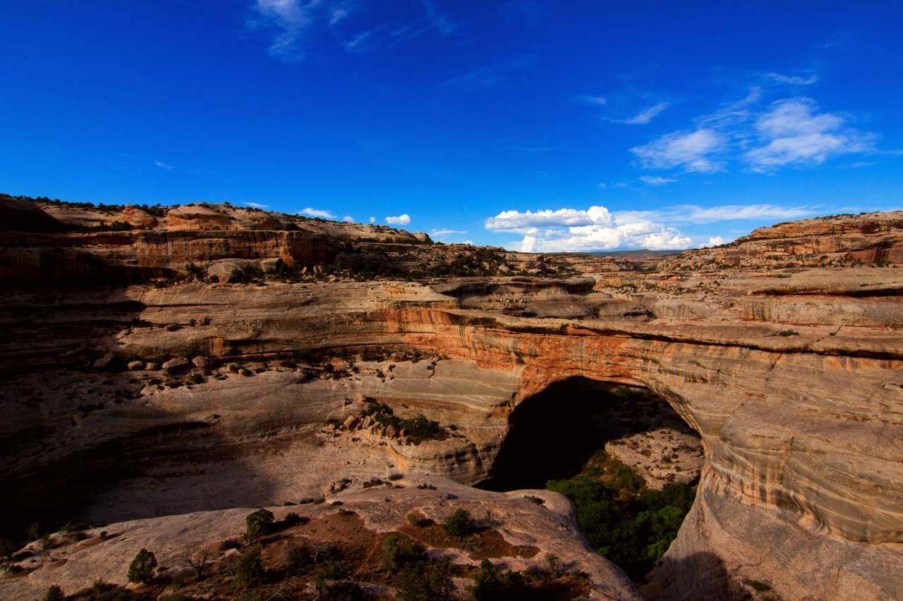 A large sandstone natural bridge with surrounding canyons and vegetation