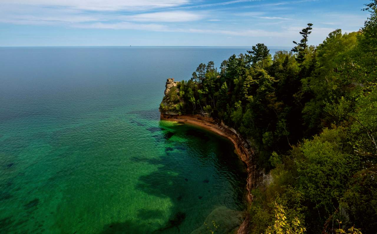 A sandstone rock formation rises out of a blue-green Lake Superior on a sunny day.