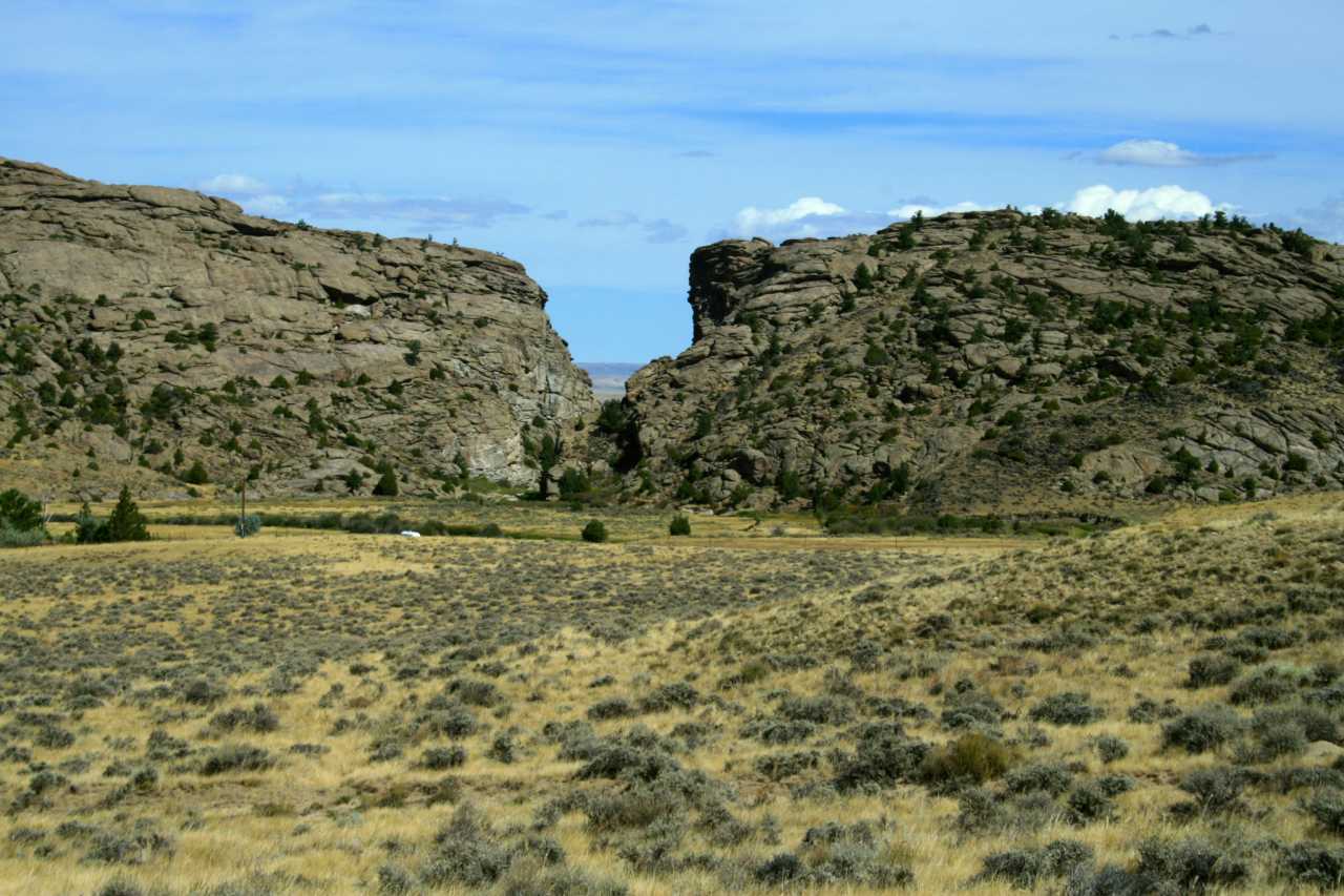 A tall rock buttress with a cleft in the center sits behind a sagebrush covered valley.