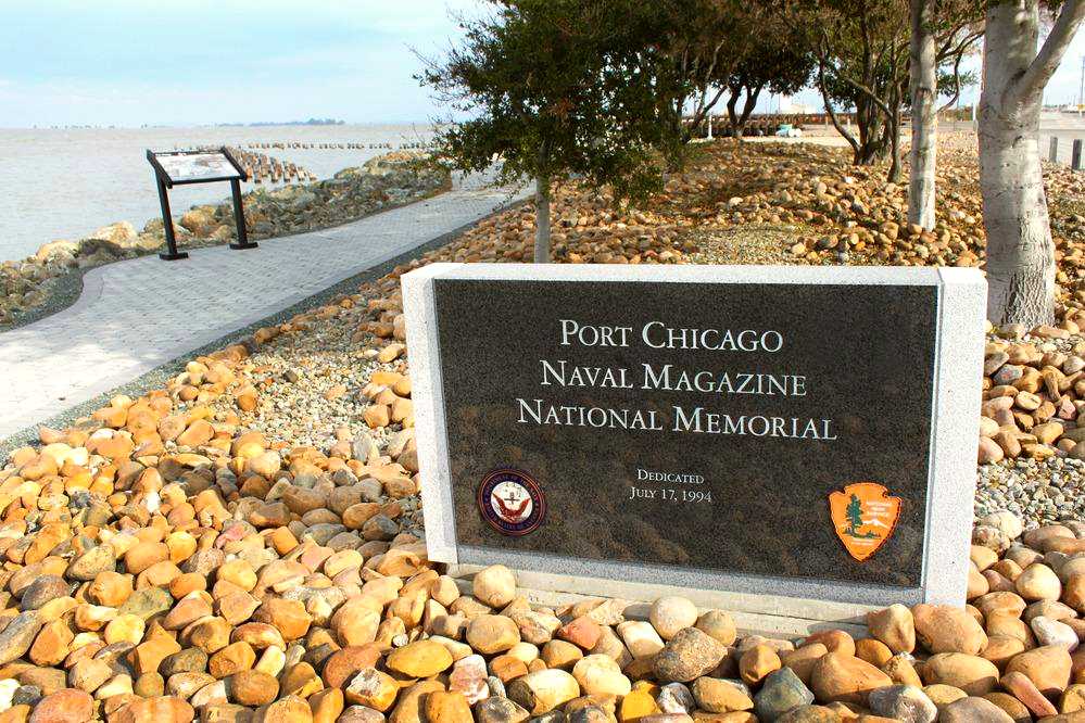 Park signs sitting in rock bed. Trees and bay in background.