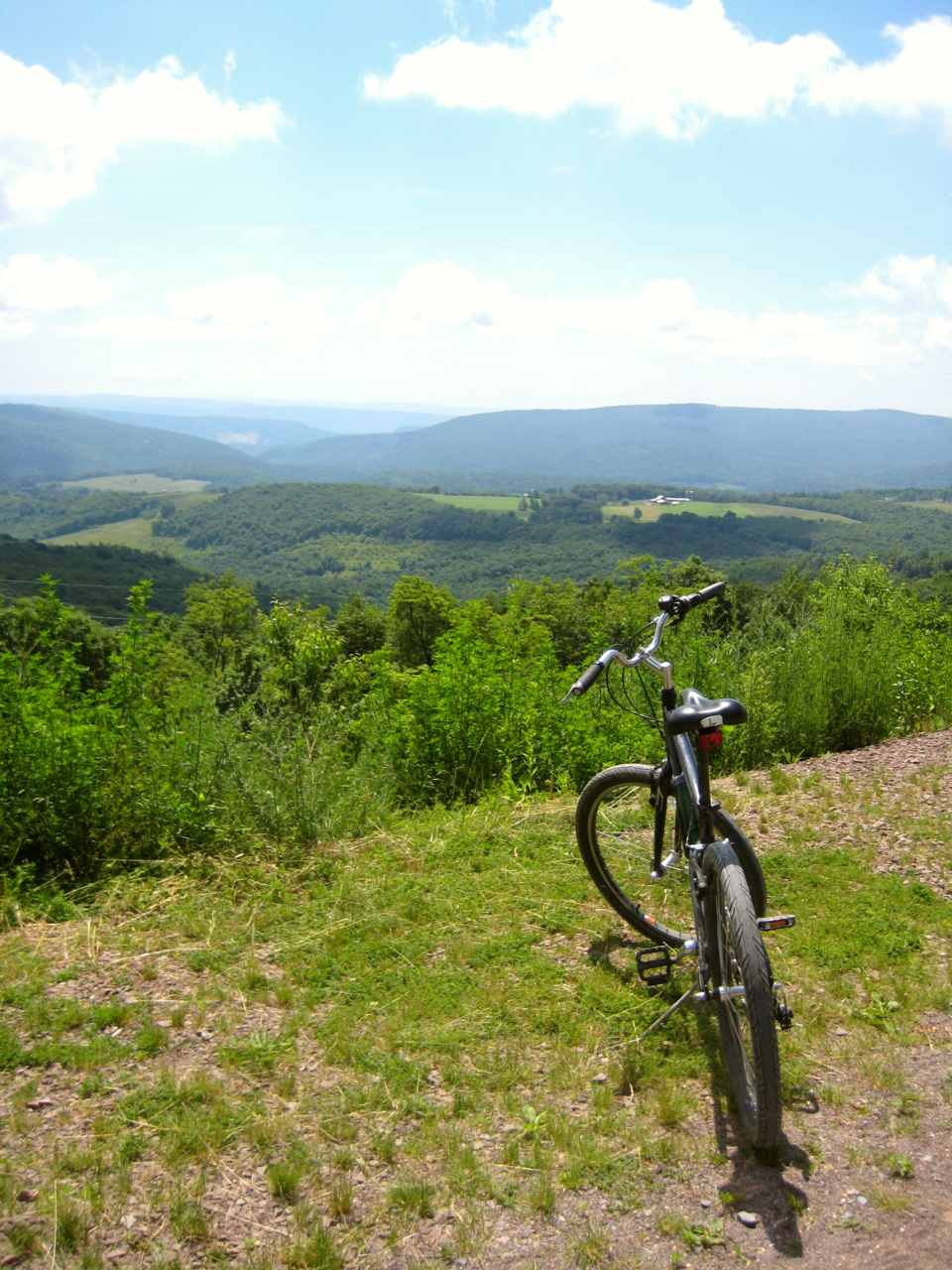 A bicycle sits on a bright summer day overlooking the rolling mountains in the distance.
