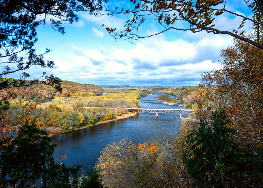 A blue river winds through a valley lined with trees in autumn color.