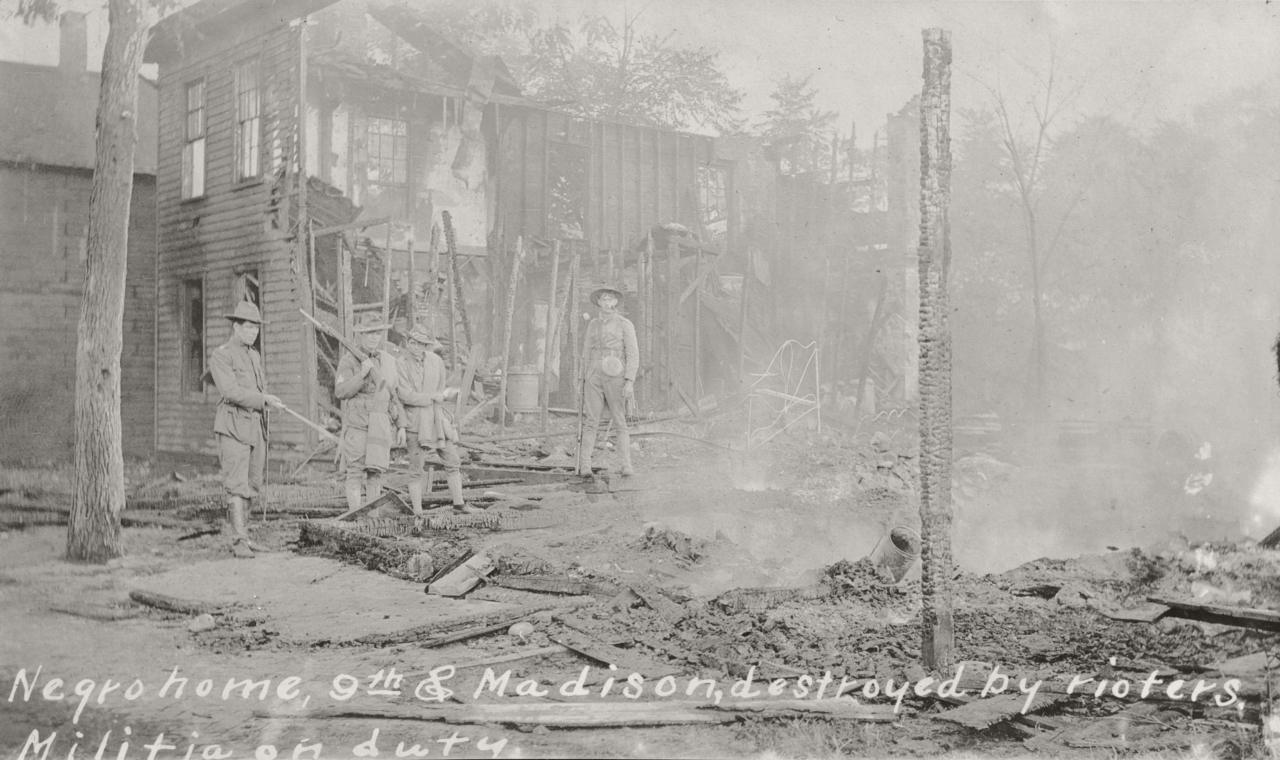 Historic photo of militia members standing in the remains of a burned building.