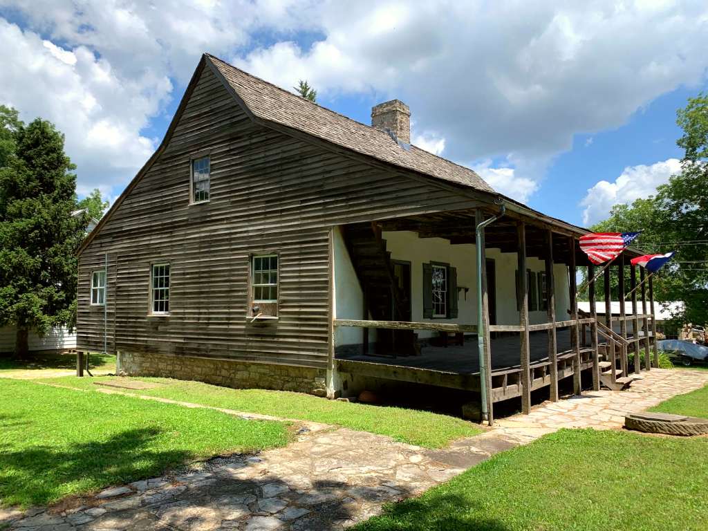 Frame house made of wood with U.S. and French flags flying on front porch.