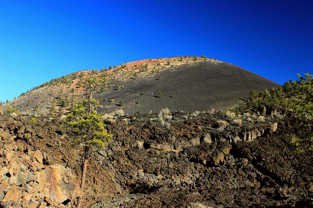a jagged field of lava beneath a cinder cone volcano