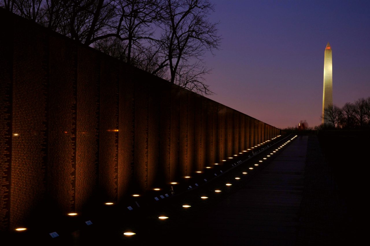 Lights glow at the base of the wall of the Vietnam Veterans Memorial with Washington Monument.