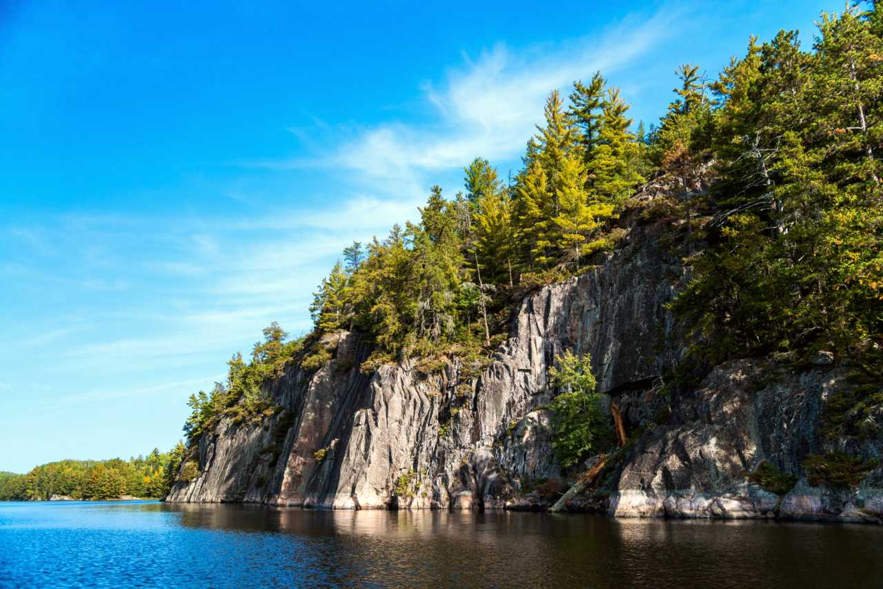 Photograph of granite cliffs topped with trees alongside a blue lake.