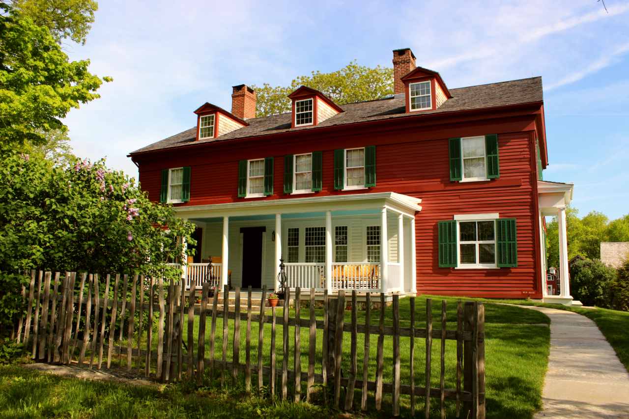A view of the south side of the Weir House with porch visable, showing a fence in front of the home