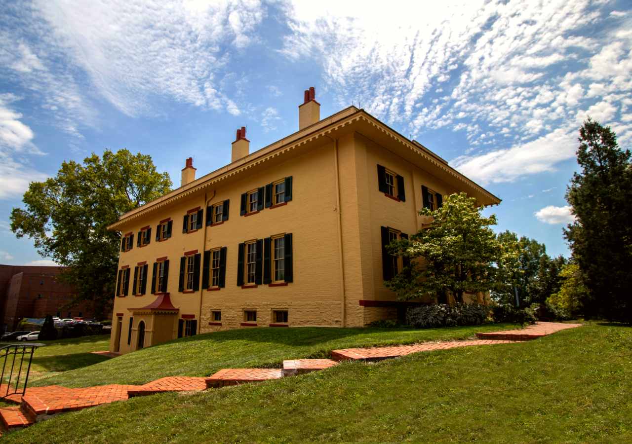 A yellow two-story brick building with tall windows and green shutters on them