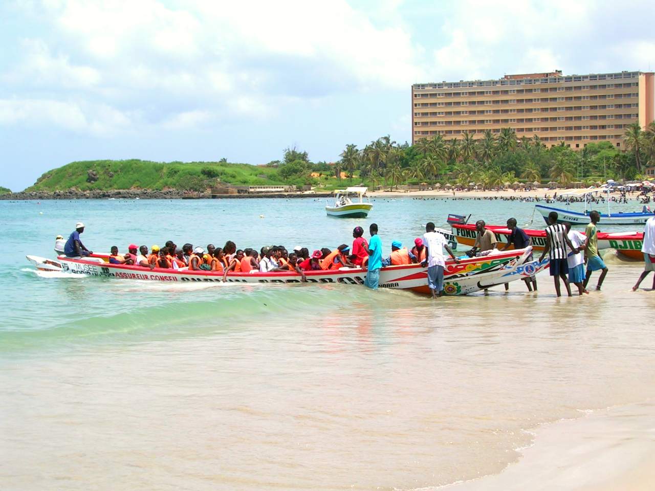 Visitors loaded into a Pirogue for a pleasure trip from Ngor to île de Ngor, a popular holiday spot for Dakar's locals. In the background is the Ngor Hotel, catering to Senegalese and business travelers to Dakar.