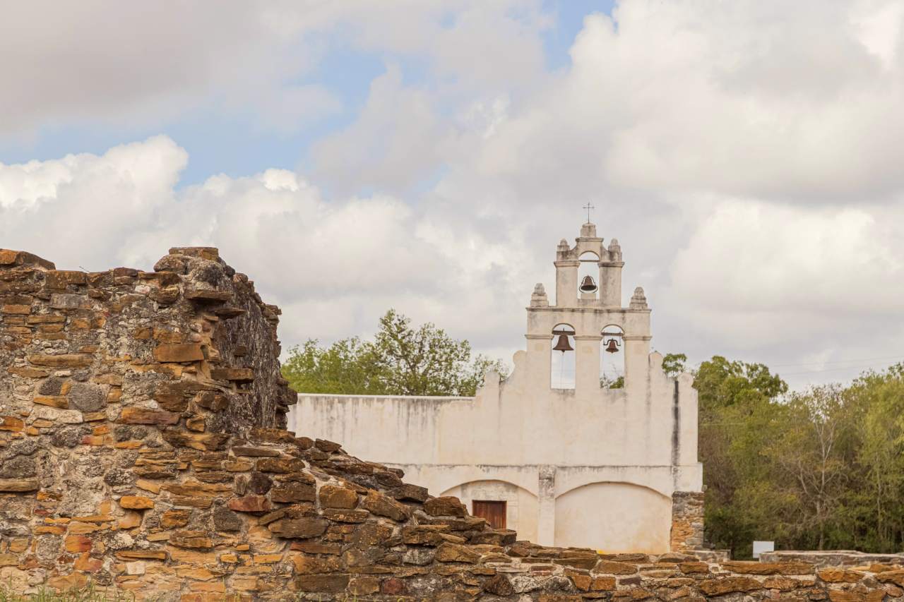 White frescoed church with a stone ruin to the left in the foreground.