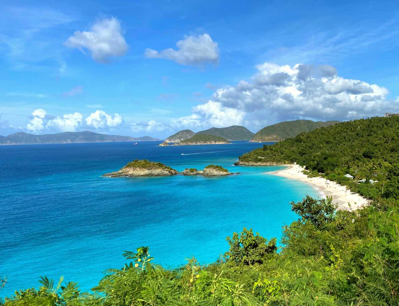 Turquoise water laps white sandy shore fringed with lush green vegetation.